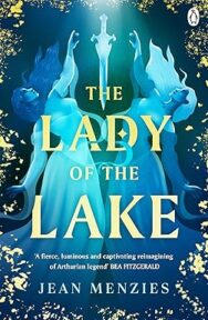 Image of a book cover featuring an illustrated blue and gold cover of two mirrored figures standing back‑to‑back, each holding one arm upward toward a glowing sword suspended vertically in the centre of the image. Decorative yellow leafy patterns frame the edges of te image. The title “THE LADY OF THE LAKE” appears in gold uppercase letters across the middle, and the author’s name “JEAN MENZIES” is printed below in white. A review quote is placed above the title which says "A fierce, luminous and captivating reimagining of Arthurian legend - Bea Fitzgerald."